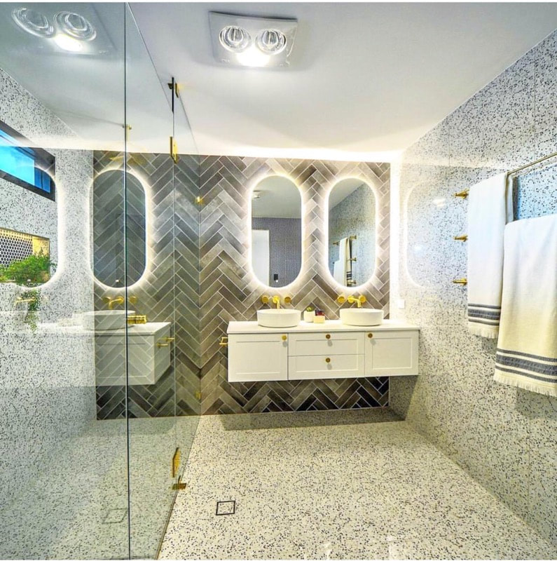 Terrazzo-tiled bathroom with dual vessel sinks and gold-framed mirrors