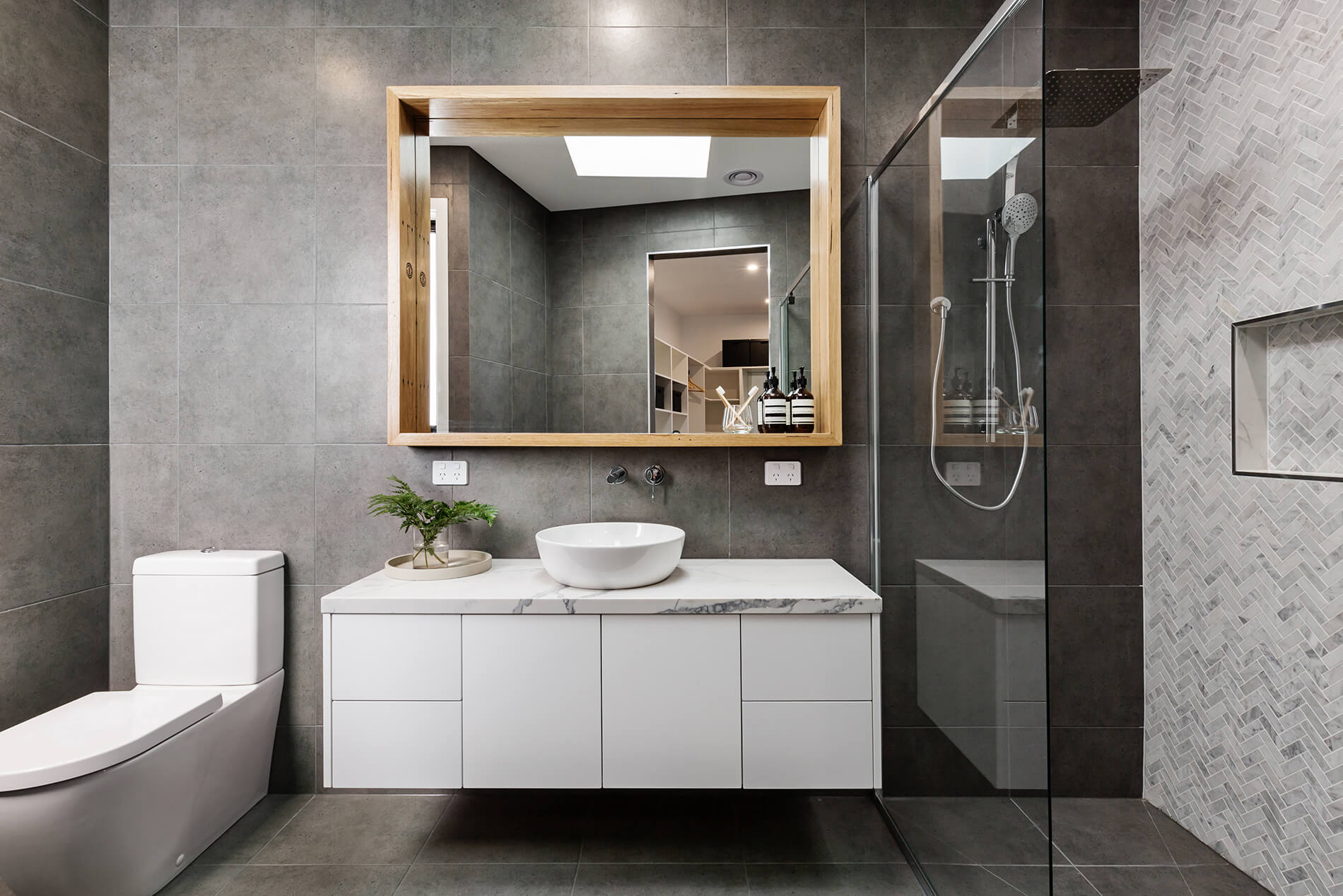 Grey-tiled bathroom with a timber-framed mirror and frameless glass shower
