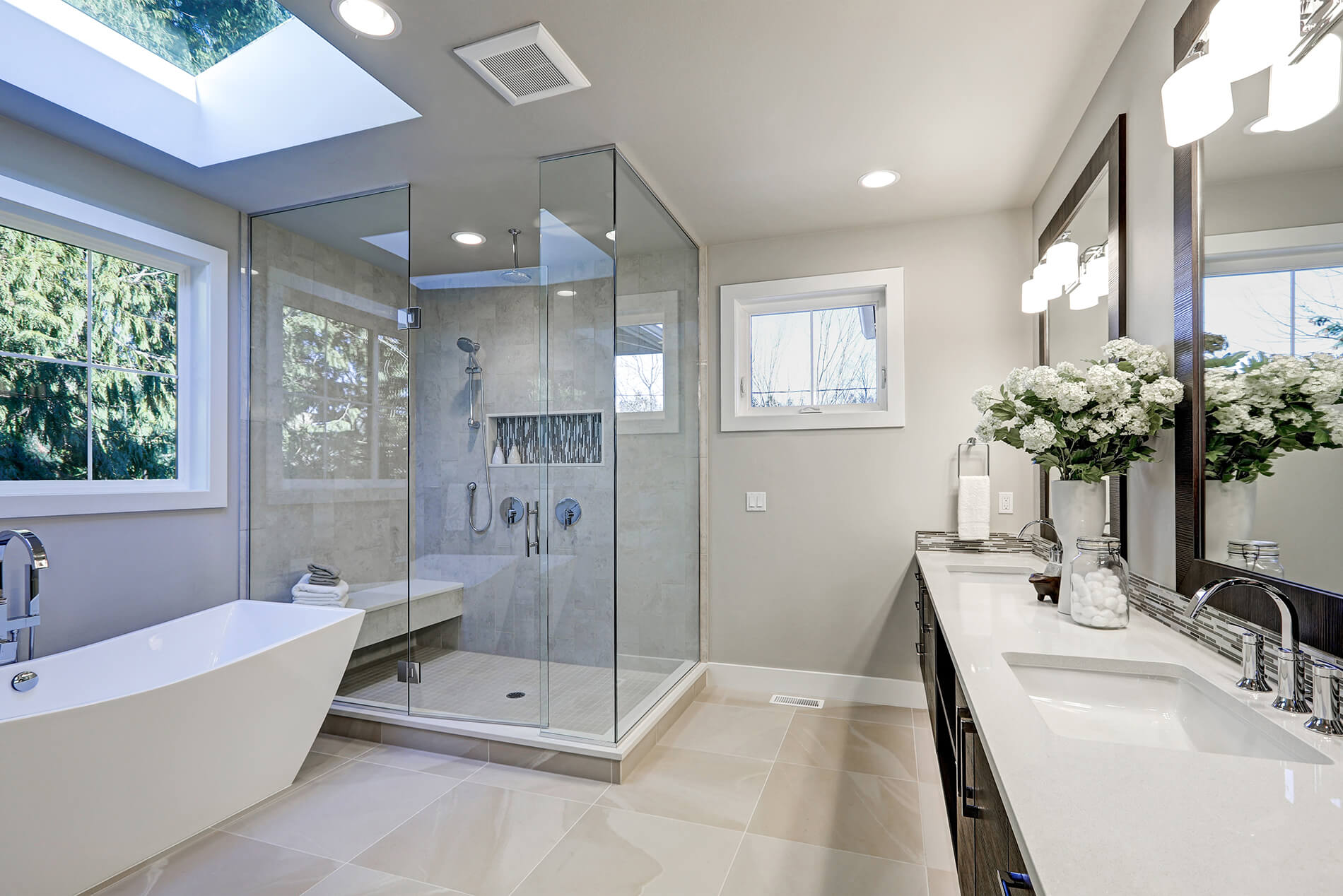 Bathroom with a skylight, frameless glass shower, double vanity, and freestanding bathtub