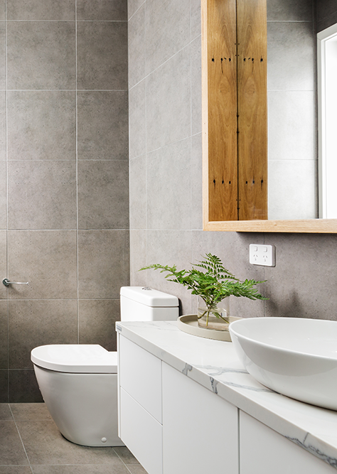 Compact en suite with a timber-framed mirror, oval vessel sink, and grey tiled walls