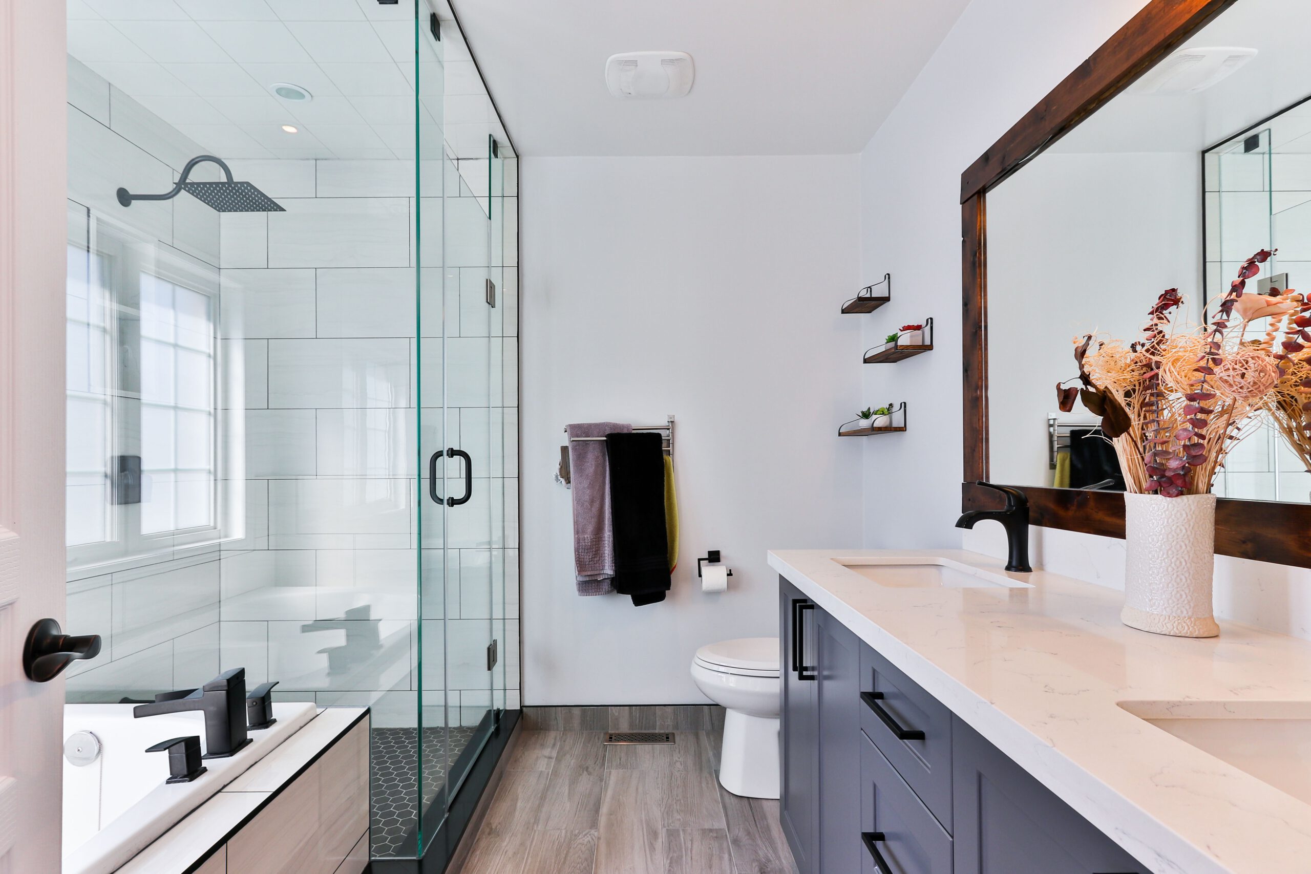 Bathroom with a frameless glass shower, timber-framed mirror, and dried floral display