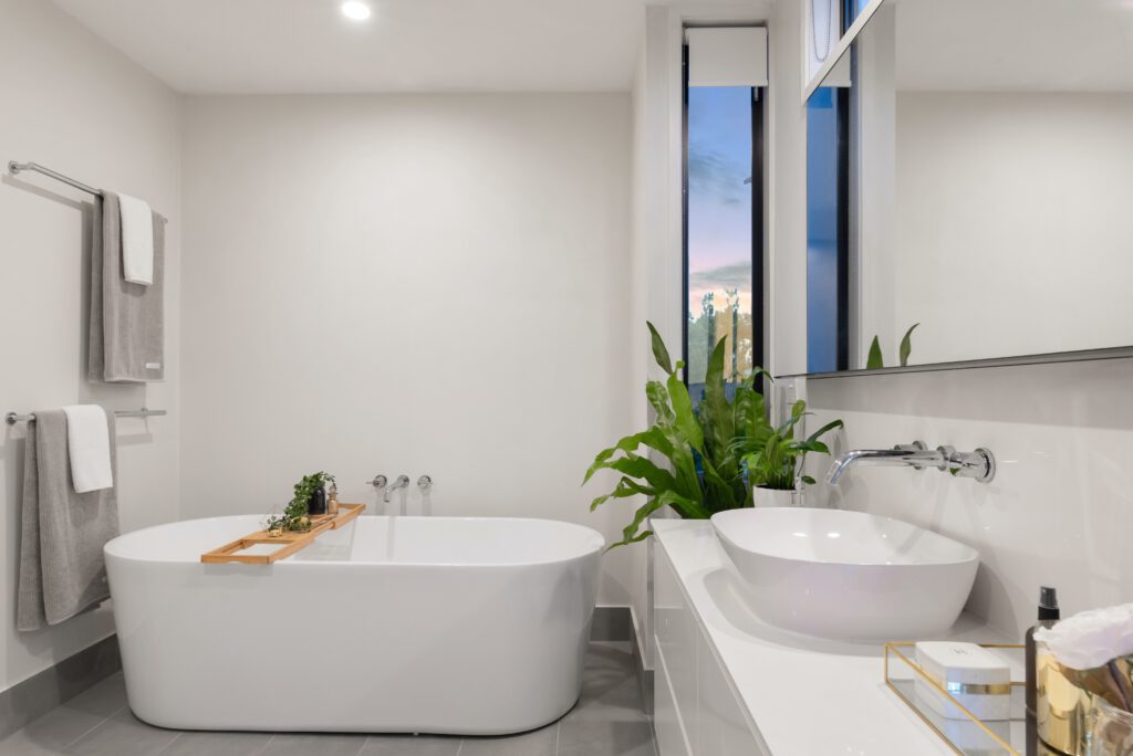 Freestanding bathtub with a wooden bath caddy, tiled feature wall, and potted plant