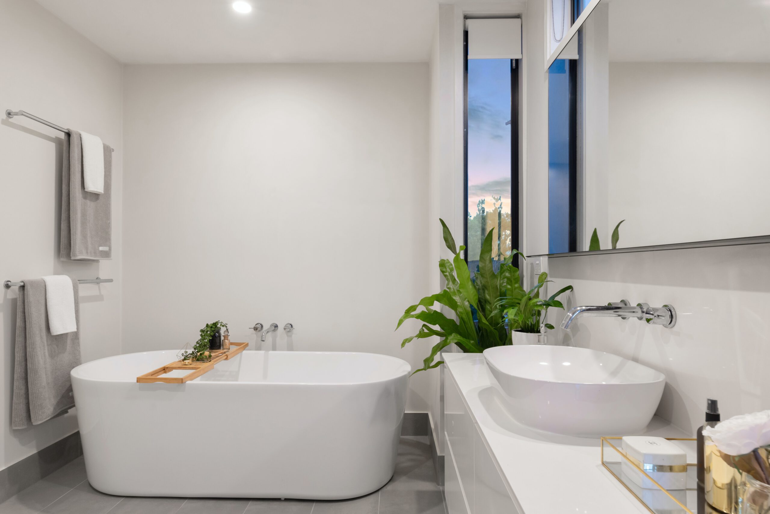 Freestanding bathtub with a wooden bath caddy, tiled feature wall, and potted plant