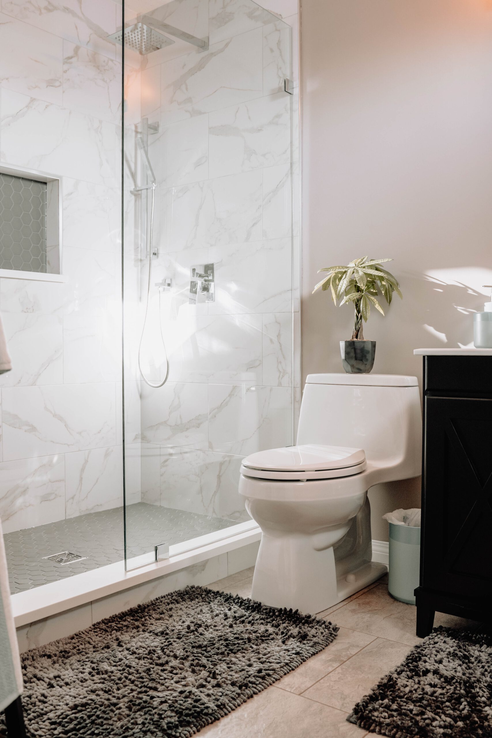 Marble-tiled walk-in shower beside a freestanding toilet and dark timber vanity