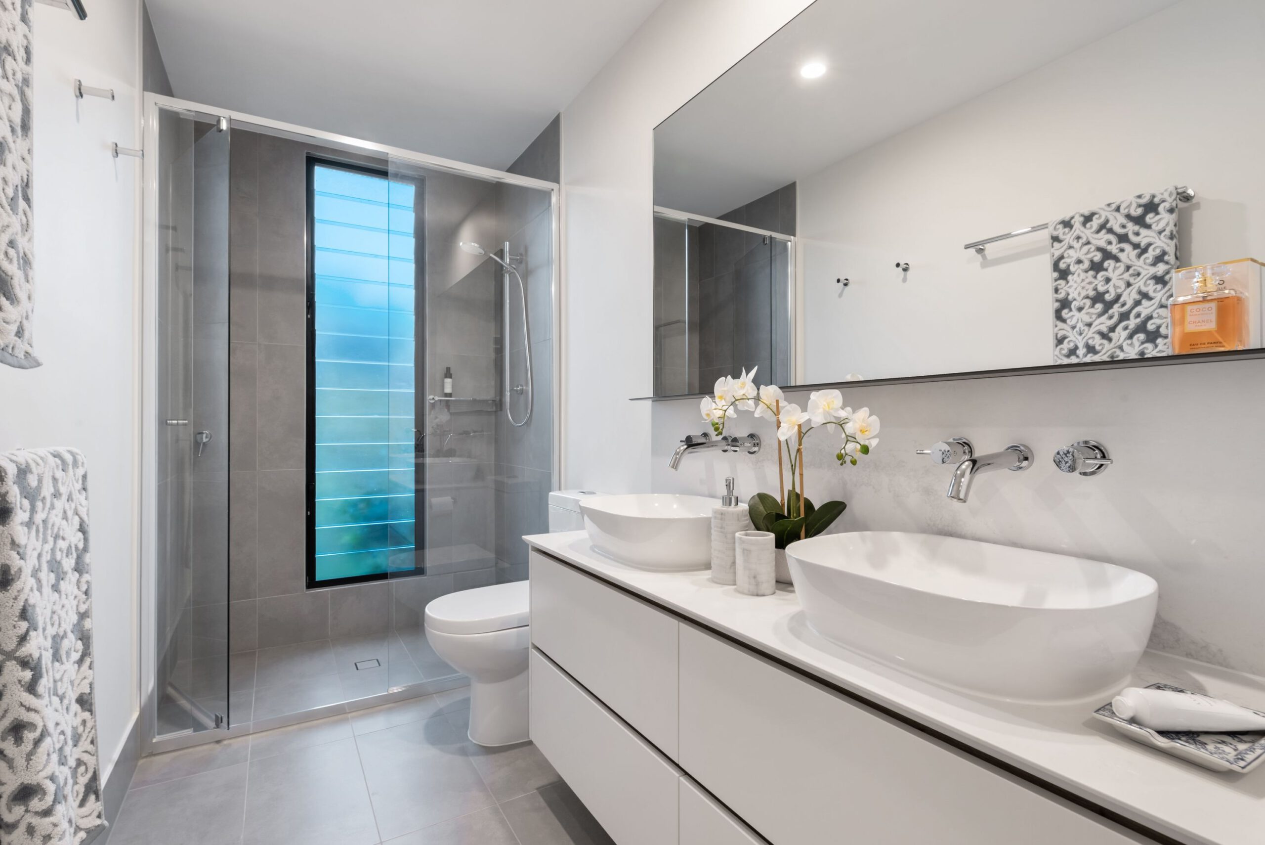 En suite with a frameless glass shower, double vessel sinks, and fresh orchids on the vanity