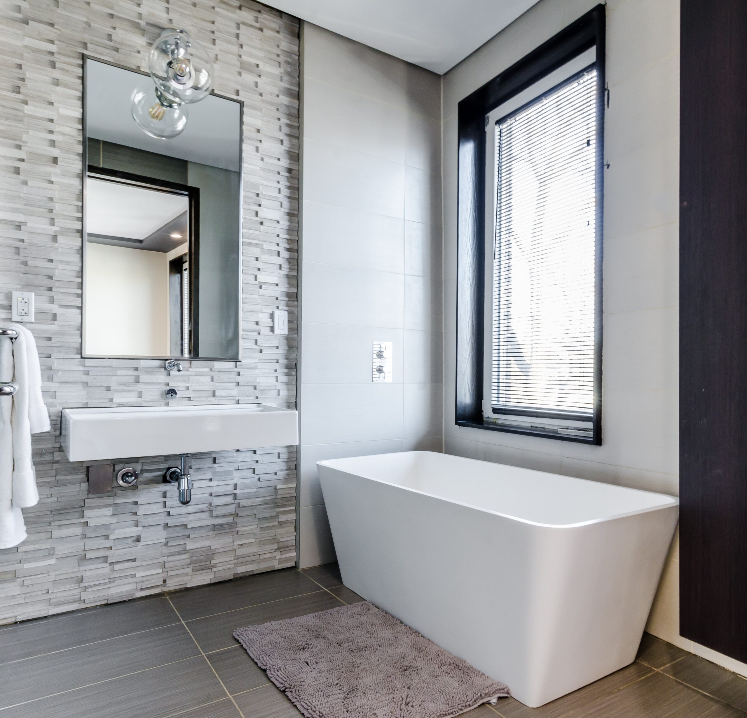 Bathroom with a mosaic tiled feature wall, wall-mounted vanity, and freestanding bathtub beside a window